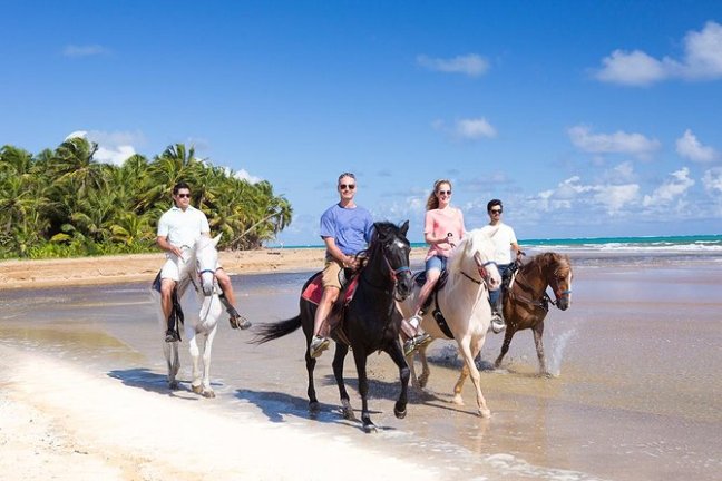 a group of people riding horses on a beach