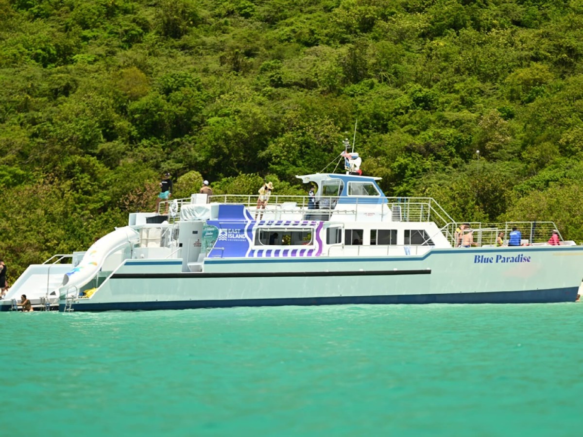 A white boat named Blue Paradise near a green forested shoreline.
