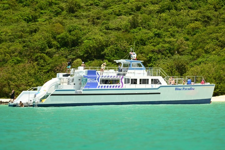 A white boat named Blue Paradise near a green forested shoreline.