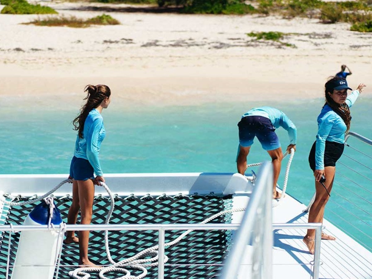 Three people on a boat near a sandy beach, wearing blue shirts.