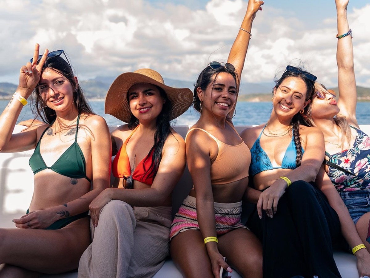 Five women in swimwear smiling and posing on a boat in sunny weather.