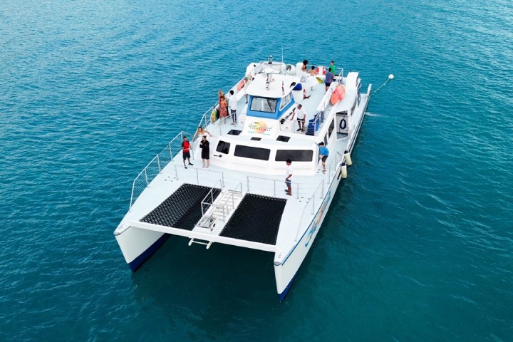 Catamaran with people on deck, sailing on calm blue water.