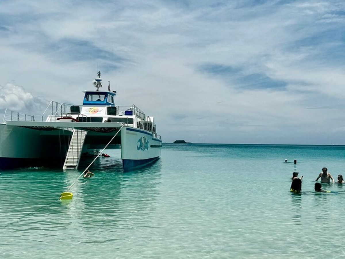 People swimming near a large white boat in clear, calm ocean waters.