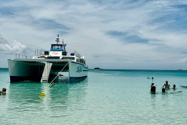 People swimming near a large white boat in clear, calm ocean waters.