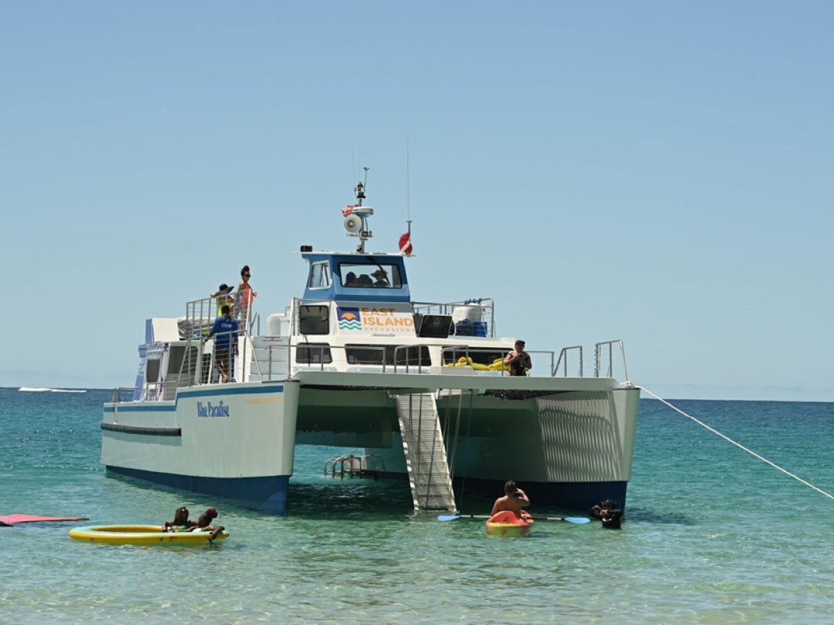 Boat anchored in clear water with people swimming nearby.