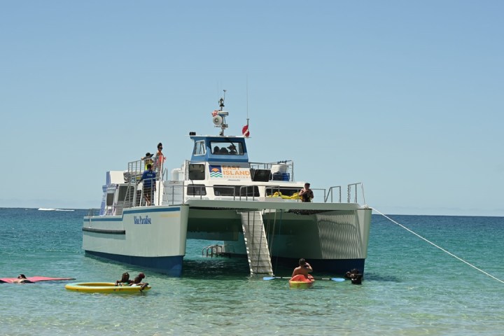 Boat anchored in clear water with people swimming nearby.