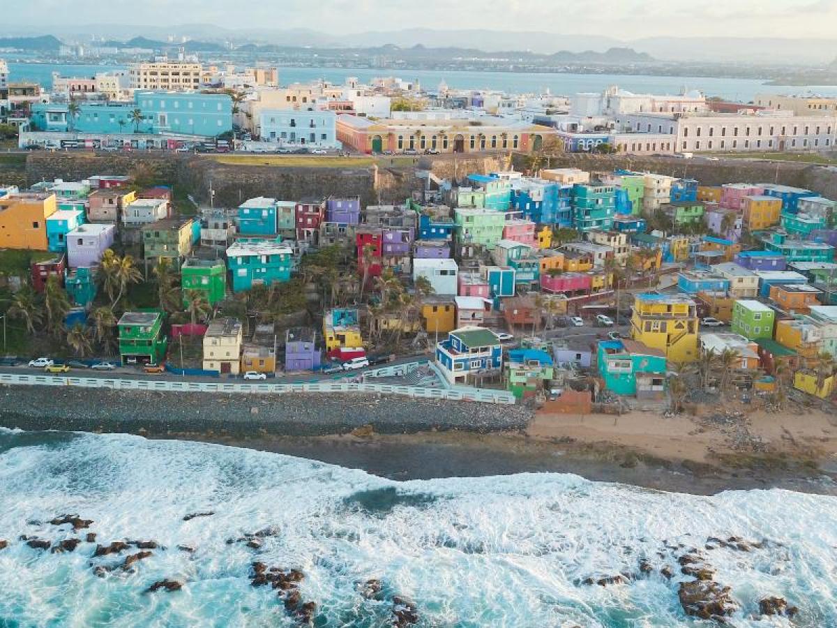 Aerial view of colorful hillside houses near the ocean with waves crashing on the shore.