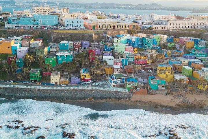 Aerial view of colorful hillside houses near the ocean with waves crashing on the shore.