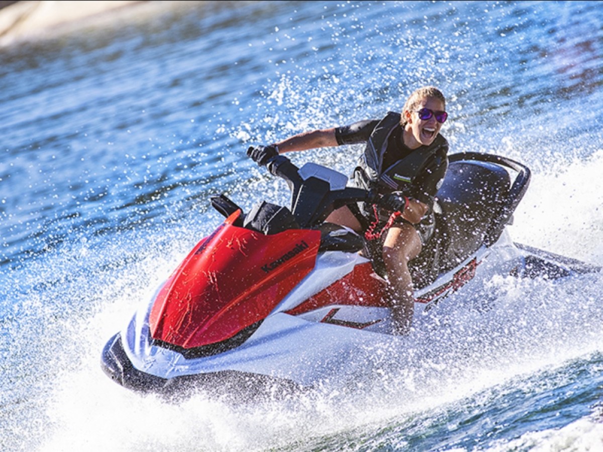 Person riding a red and white jet ski on water, creating splashes.