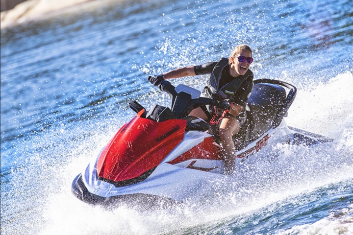 Person riding a red and white jet ski on water, creating splashes.