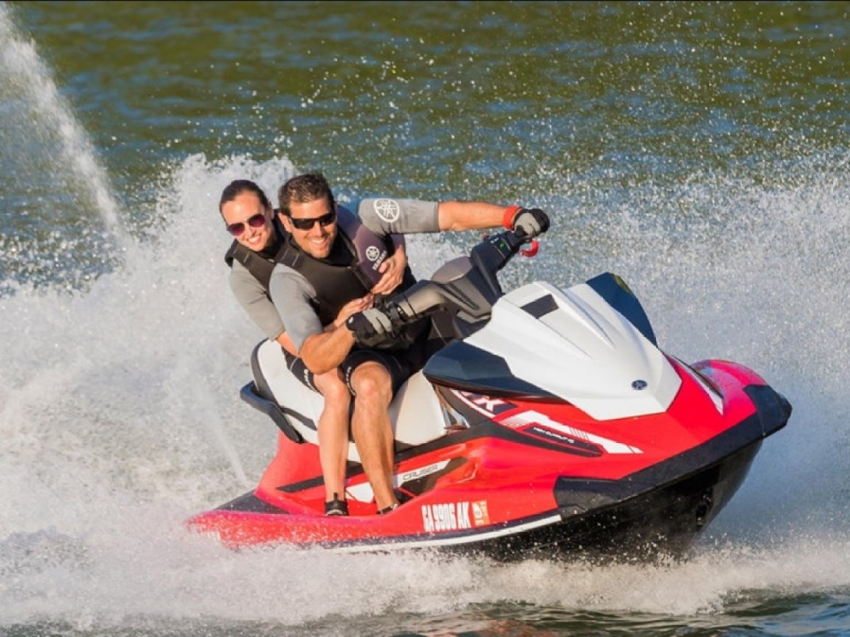 Two people riding a red and white jet ski on a lake, creating splashes behind them.