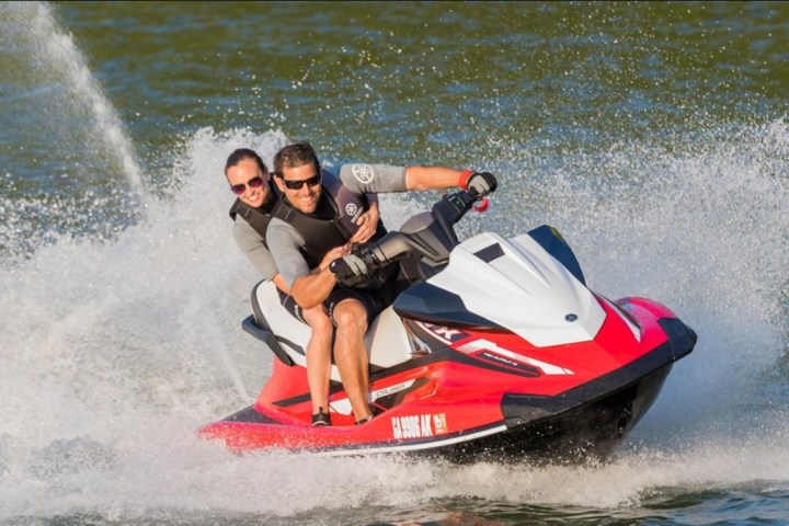 Two people riding a red and white jet ski on a lake, creating splashes behind them.