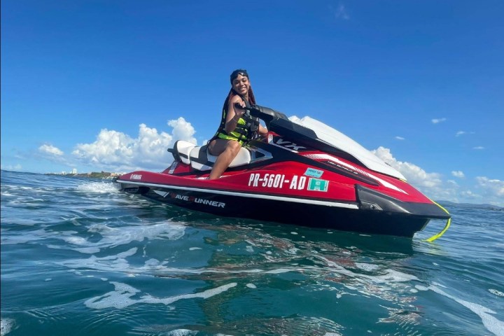 Person on a red jet ski on the ocean with a blue sky and clouds in the background.