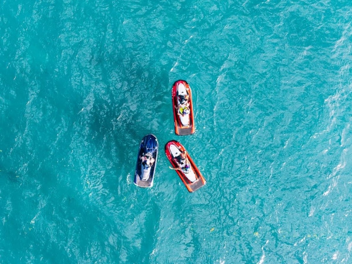 Three people on jet skis in blue ocean viewed from above.