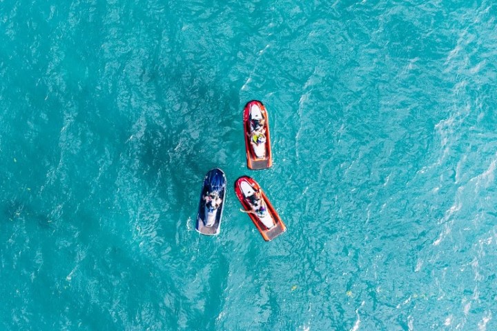 Three people on jet skis in blue ocean viewed from above.
