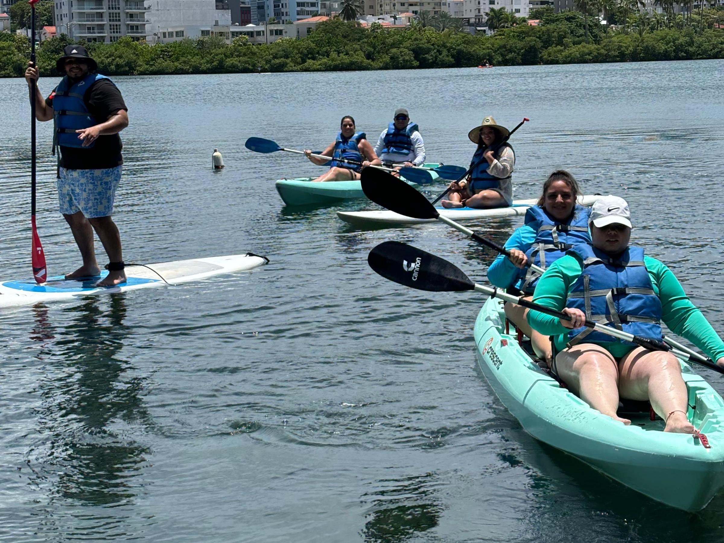 People kayaking and paddleboarding on a lake with city skyline in background.