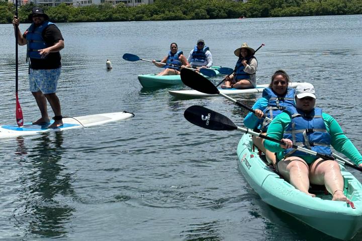 People kayaking and paddleboarding on a lake with city skyline in background.