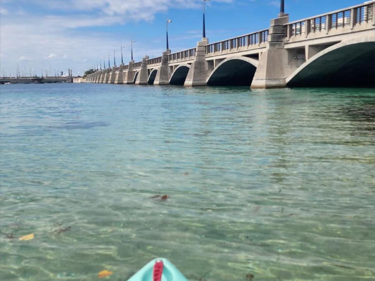 Kayak on clear water near a bridge with blue sky.