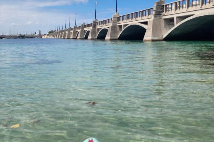 Kayak on clear water near a bridge with blue sky.