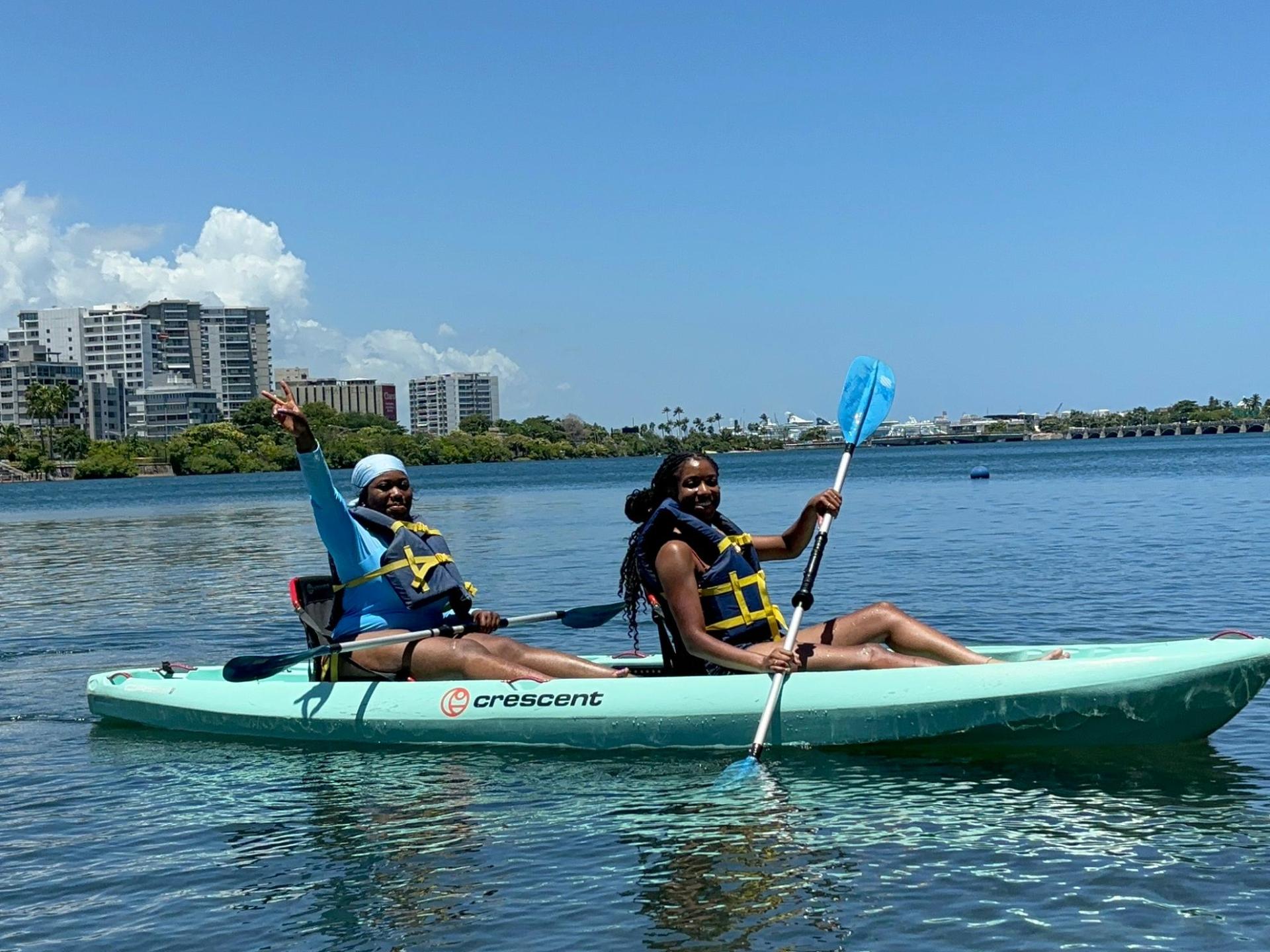 Two people kayaking on calm water under a clear blue sky.