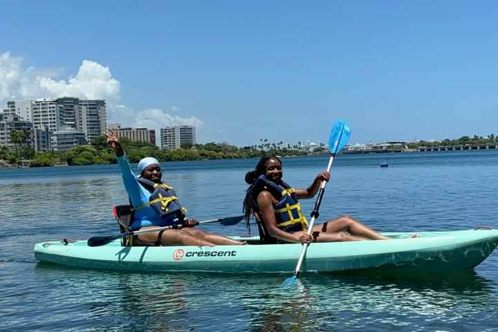 Two people kayaking on calm water under a clear blue sky.