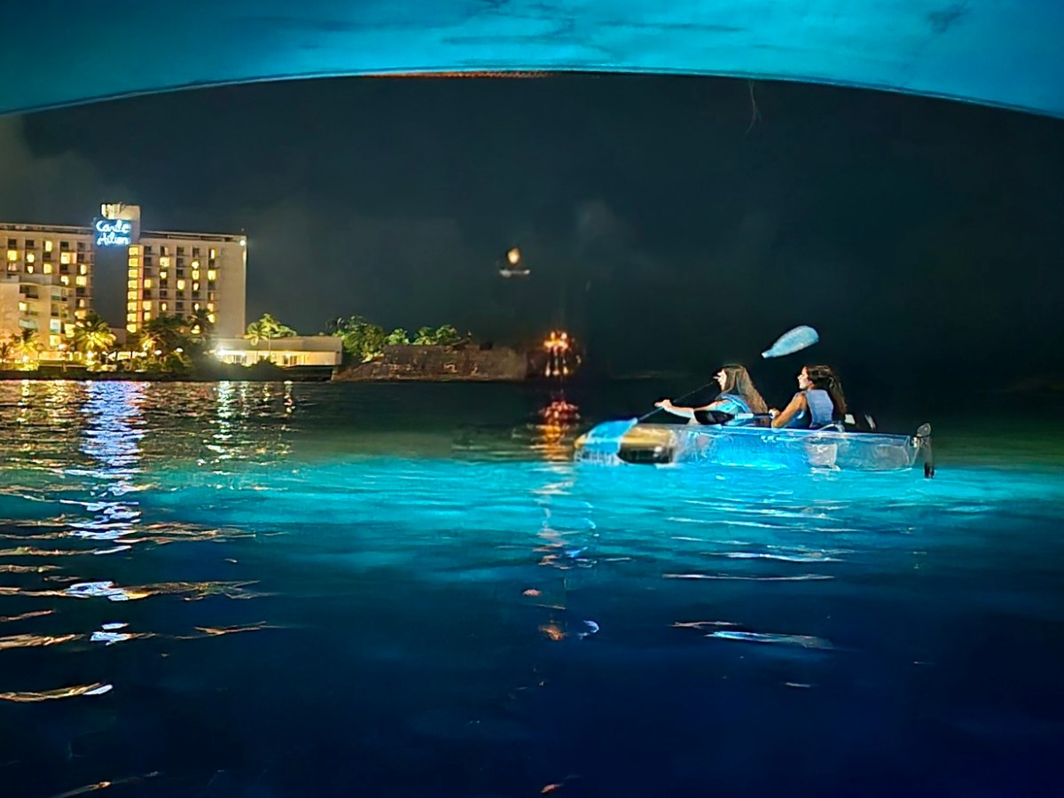 Two people kayaking at night near a lit-up building on the water.