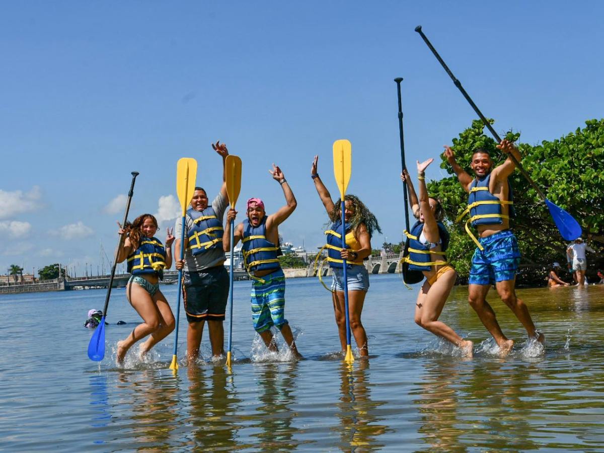 Group of people in life vests with paddles joyfully playing in shallow water.
