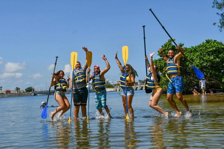 Group of people in life vests with paddles joyfully playing in shallow water.