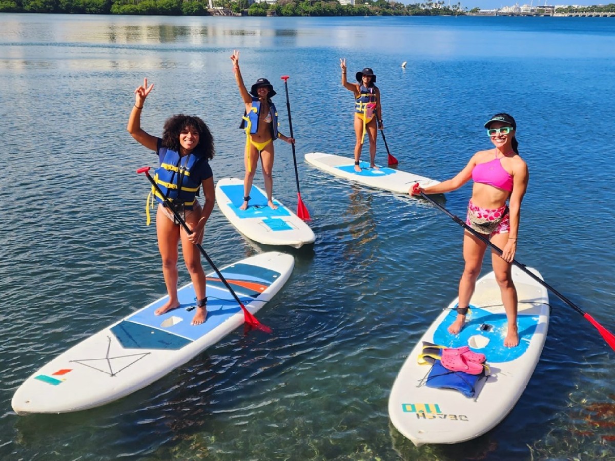 Four people paddleboarding on a calm lake, smiling and posing.