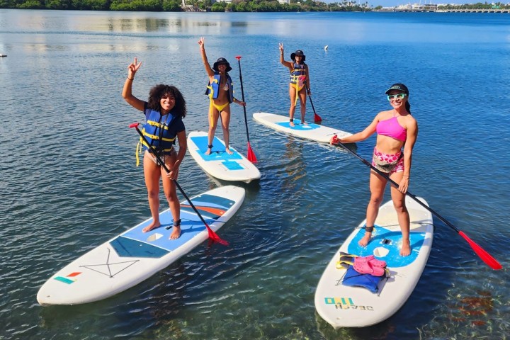 Four people paddleboarding on a calm lake, smiling and posing.