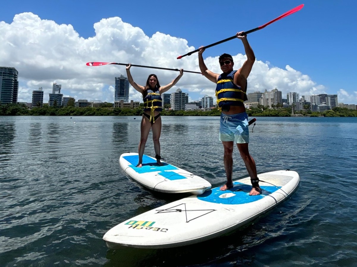 Two people on paddleboards raising paddles, with city skyline in background.