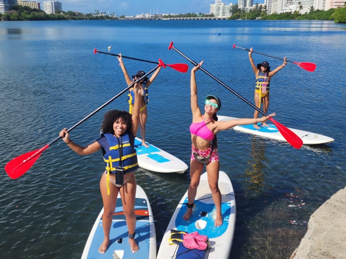 Four people on paddleboards, holding paddles aloft, on a sunny day by the water.