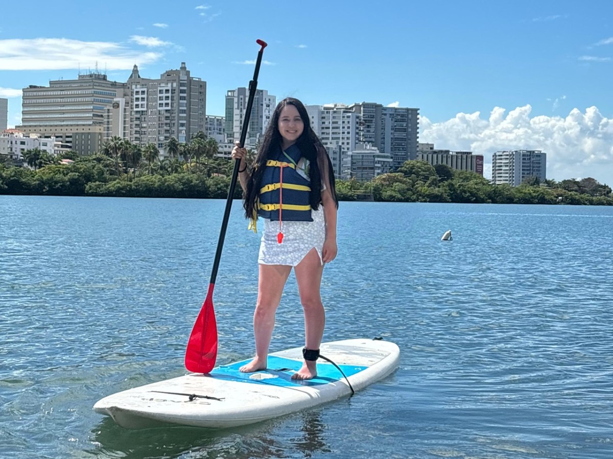 Person paddleboarding on calm water with city skyline in background on a sunny day.