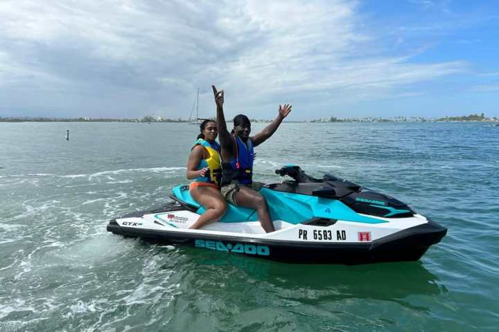 Two people on a jet ski in calm waters with cloudy sky.