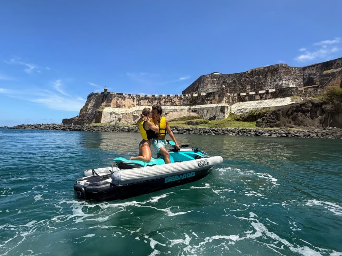 Couple on jet ski in front of historic fortress by the ocean on a sunny day.