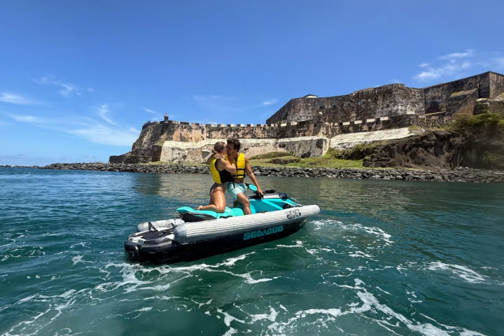 Couple on jet ski in front of historic fortress by the ocean on a sunny day.