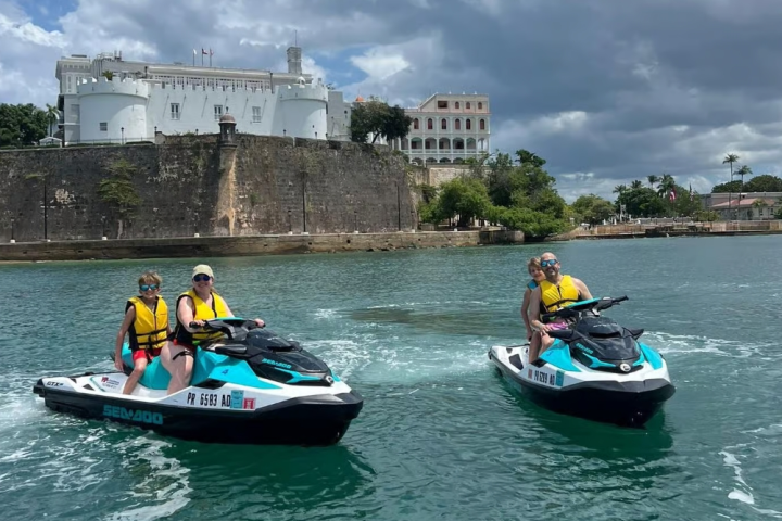Two jetskis with people wearing life jackets in front of a historic fortress on a sunny day.