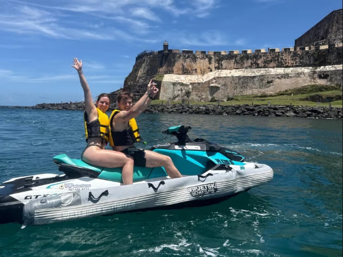 Two people on a jet ski near a historic fort on a sunny day.