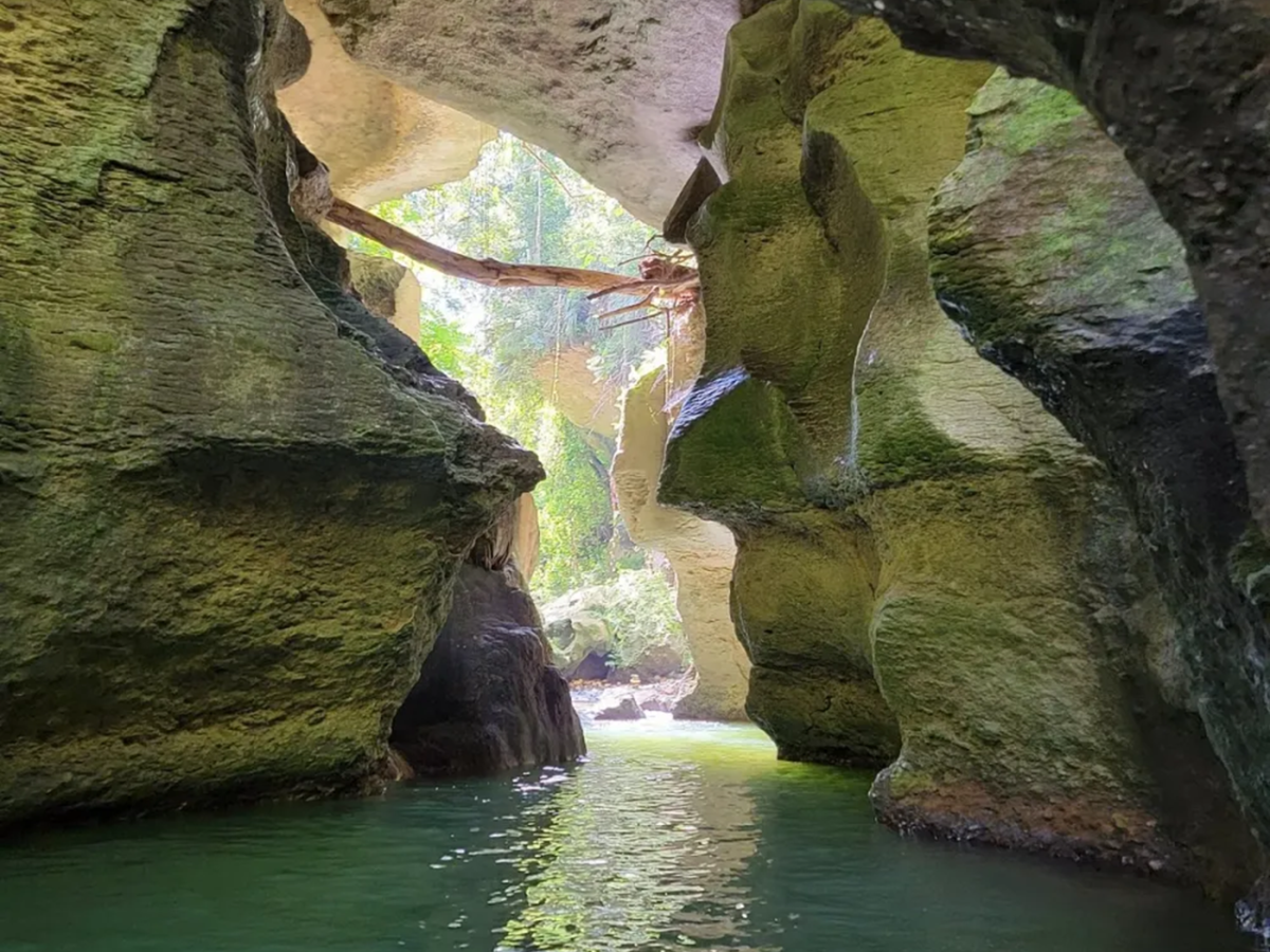View inside a rocky cave with sunlight and water below.