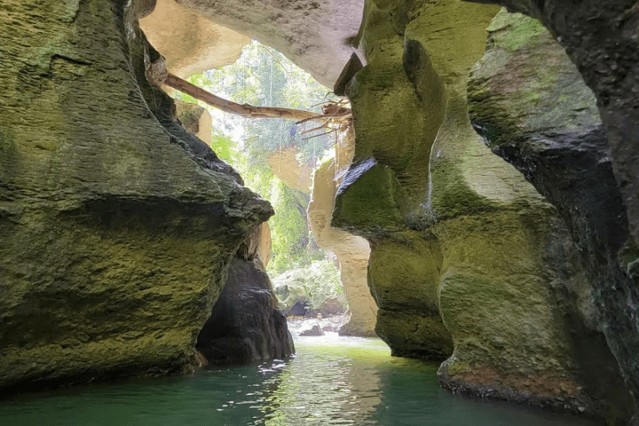 View inside a rocky cave with sunlight and water below.