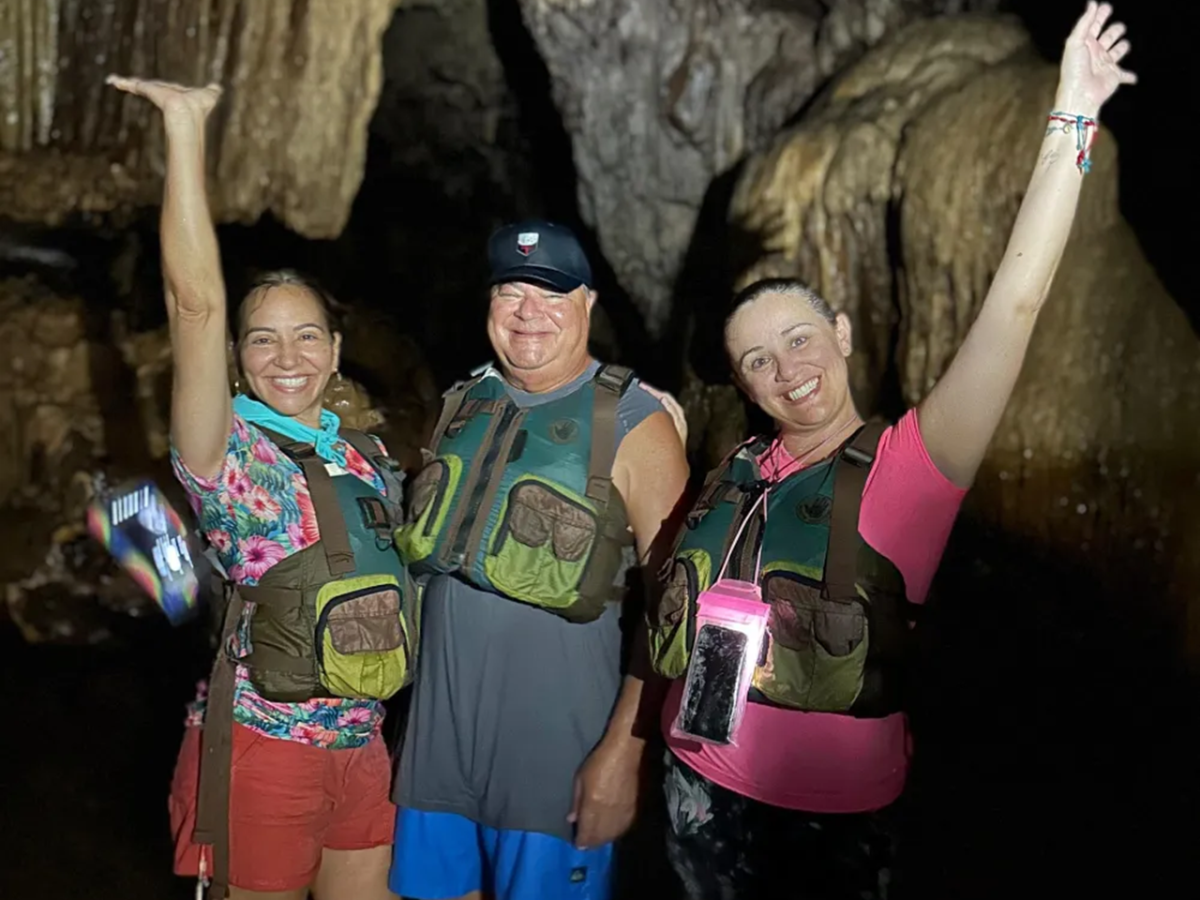 Three people in life vests posing inside a cave with raised arms.