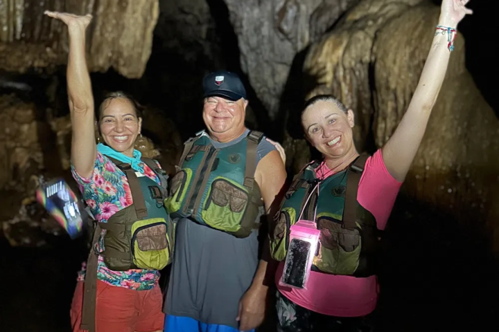 Three people in life vests posing inside a cave with raised arms.