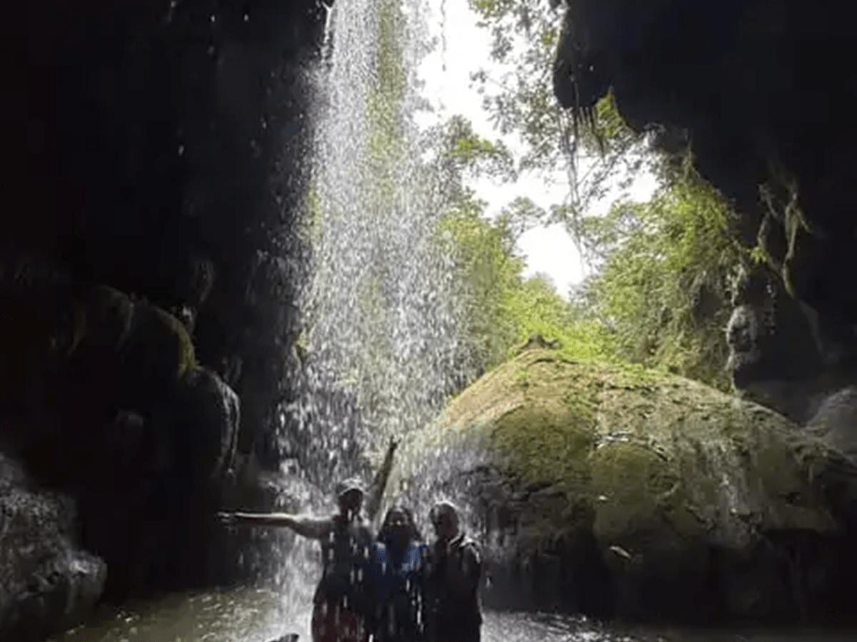 Three people under a small waterfall in a cave.