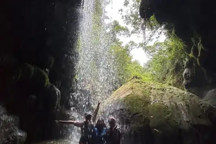 Three people under a small waterfall in a cave.