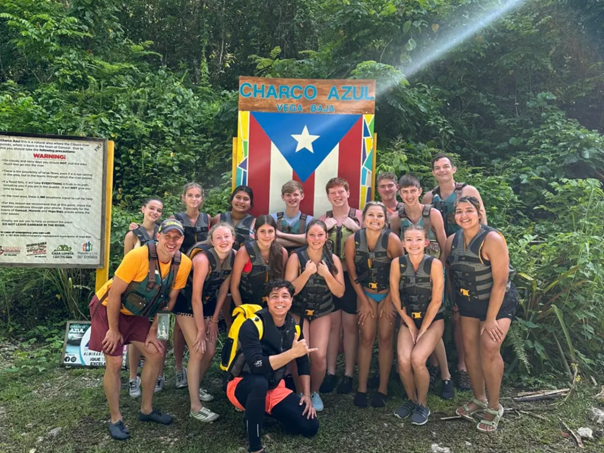 Group of people in life jackets posing at Charco Azul sign in a forested area.