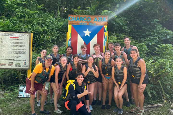 Group of people in life jackets posing at Charco Azul sign in a forested area.