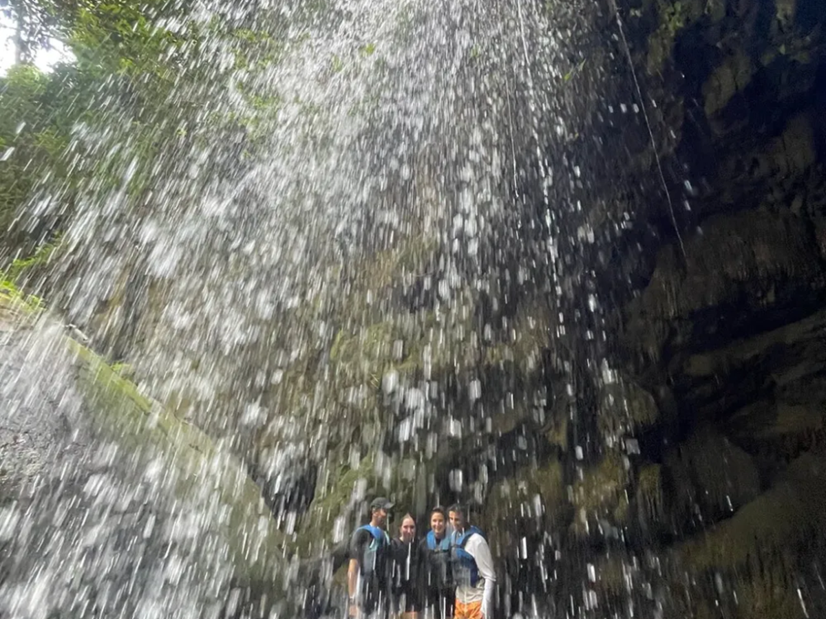 People standing behind a waterfall in a rocky area.