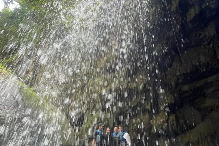 People standing behind a waterfall in a rocky area.