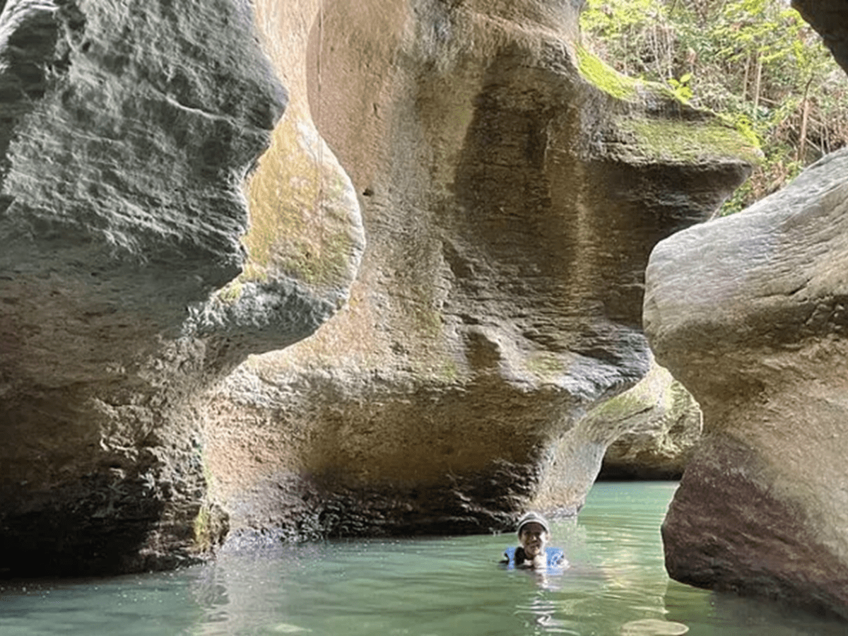 Person swimming in a rocky canyon with tall, mossy walls.