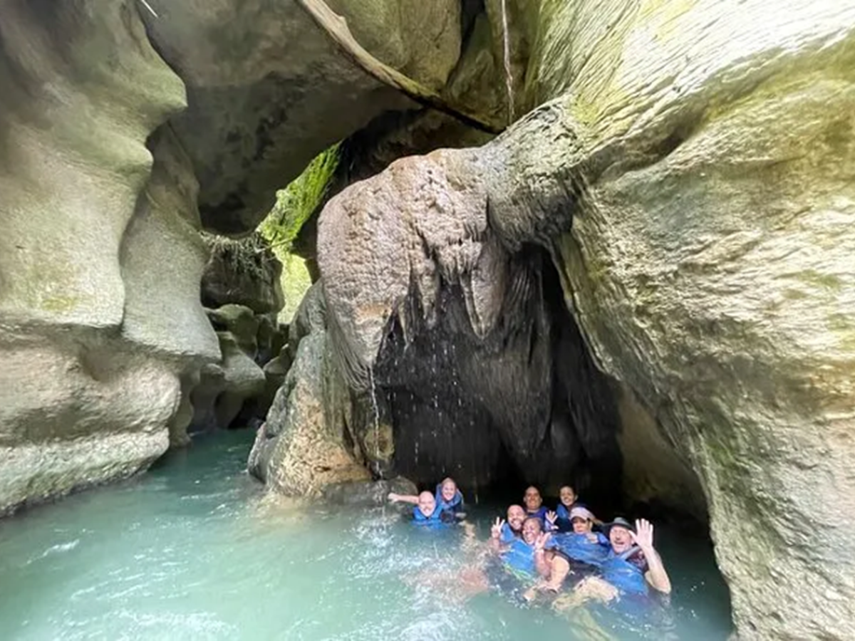 Group of people in a rocky cave with water, smiling and waving.